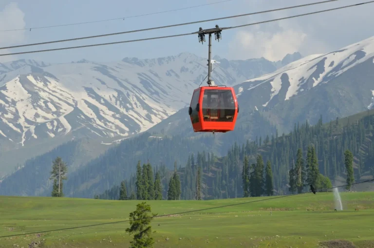 Red Gulmarg Gondola cabin above green meadows and snowy peaks in summer